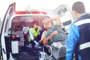A car accident victim with a common brain injury caused by an auto accident is being loaded into an ambulance by two rescue workers.
