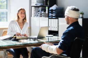 A lawyer sits across from her injured client, who has a bandage around his head and a cast on his arm. She explains what to do after an electric scooter accident in Wisconsin.